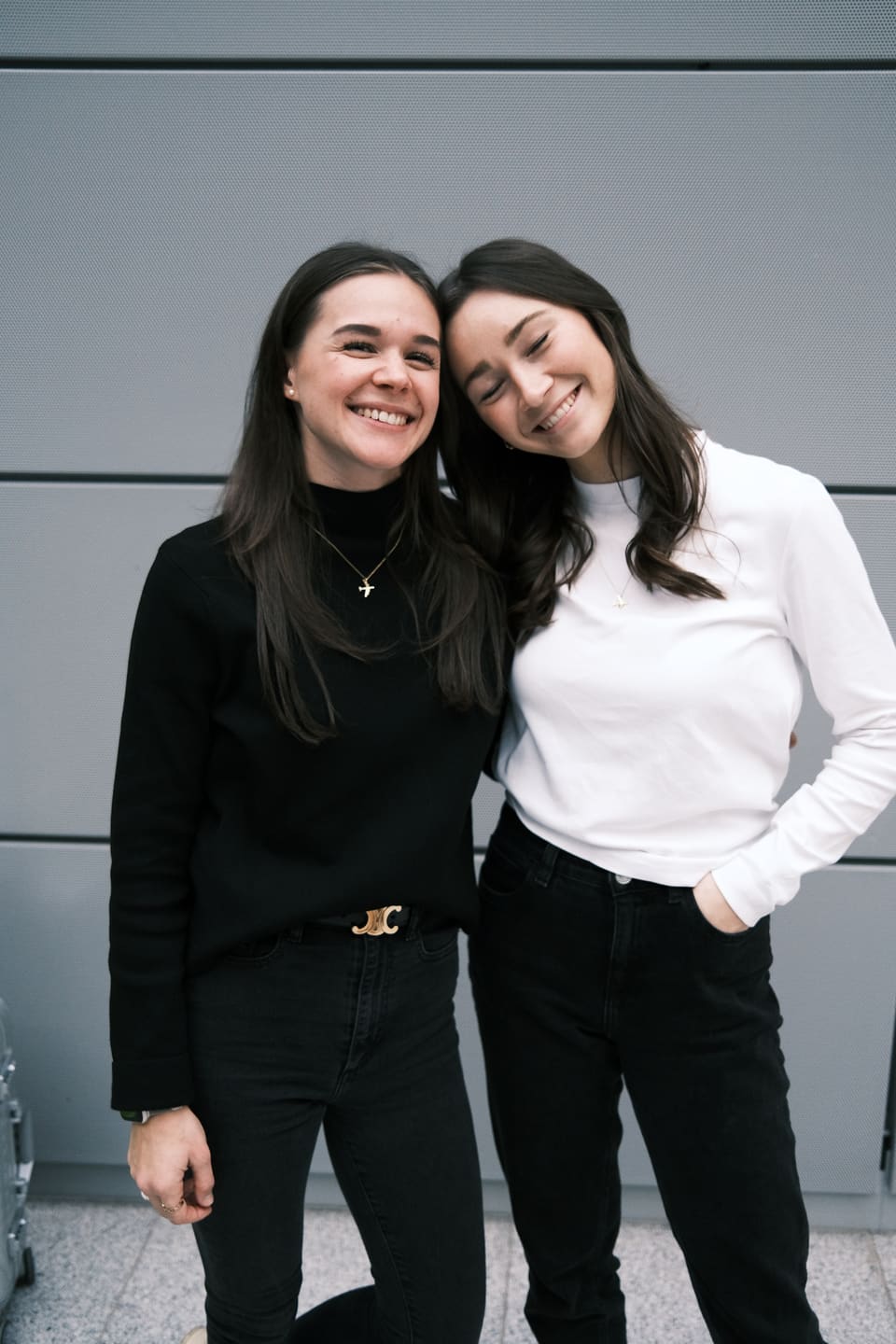Porträt von Anna und Julia: Kopf an Kopf, beide strahlen in die Kamera, eine in Schwarz, eine in Weiß.