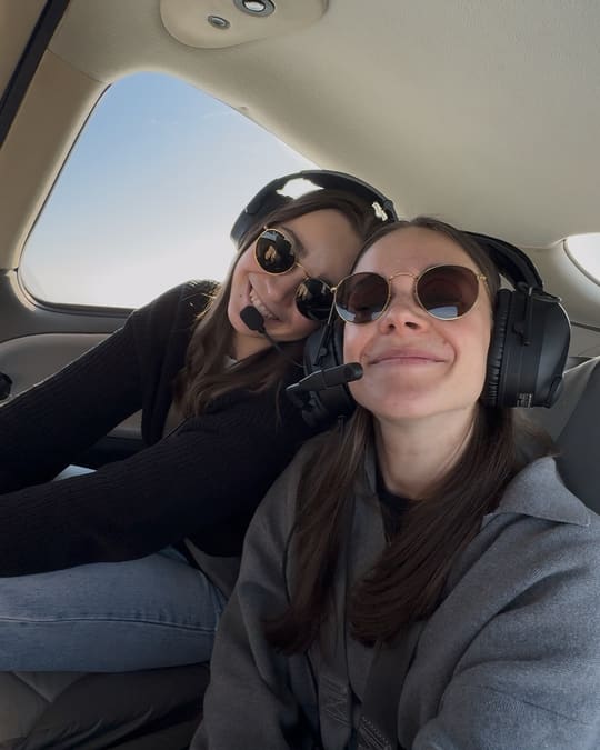Selfie von Anna und Julia im Cockpit eines kleinen Flugzeugs, beide mit Headsets und Sonnenbrillen.